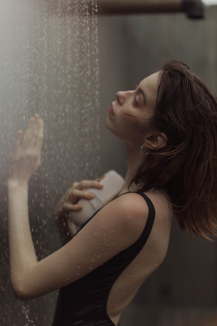 Young woman in swimwear embracing relaxation under falling water in an outdoor shower.